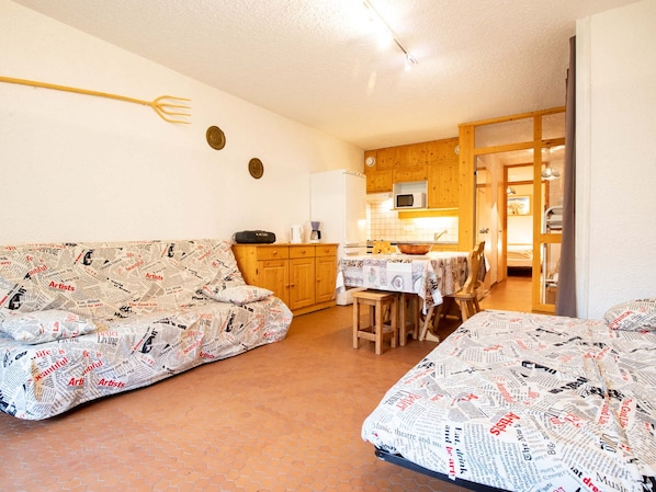 Ein gemütliches Wohnzimmer mit einer Couch und einem Esstisch, eine Küche mit Holzschränken und einer Tür zu einem anderen Raum.