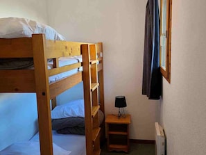 A bunk bed room with a small bedside table and a window with curtains. - Studio cabin mountain view - 4 guests (Valfréjus)