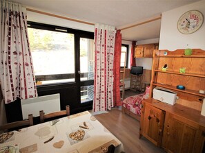 A compact kitchen with a dining table, wooden cabinets, a built-in stove, and a window with curtains. - Studio cabin at the edge of the woods - 4 guests (Villarodin-Bourget)