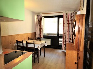 A compact kitchen with a wooden table, chairs, a stove, and a window with curtains. - Studio cabin at the edge of the woods - 4 guests (Villarodin-Bourget)