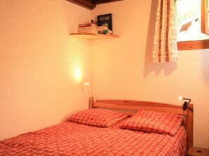 Une chambre à coucher avec un lit, des oreillers, une table de chevet, une étagère murale avec des livres et une fenêtre avec des rideaux.