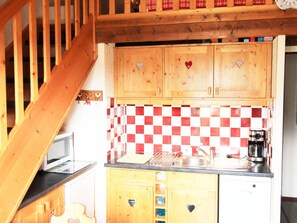 Eine Küche mit Holzausstattung, einer karierten Spritzschutzleiste, einer Mikrowelle, einer Kaffeemaschine und einer Holztreppe.