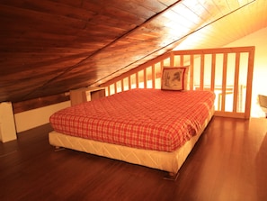 Ein Schlafzimmer mit geneigter Decke, einem Bett mit rot kariertem Überwurf und einem Holzkopfstück.