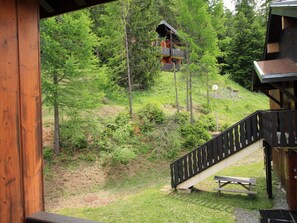 Eine Holzhütte mit einer Treppe, die zu einer Terrasse führt, umgeben von dichtem Wald.