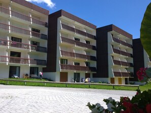 Un hotel de diverses plantes amb balcons, un pati empedrat i un cel serè.