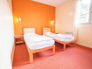 Habitació amb dos llits individuals, un radiador i una finestra amb cortines.