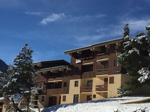 Un immeuble à plusieurs étages doté de balcons, entouré d’arbres couverts de neige.