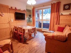 Ein gemütliches Zimmer mit Holzvertäfelung, einem Esstisch mit Stühlen, einem Sofa, einem Fernseher und einem Fenster mit Vorhängen.