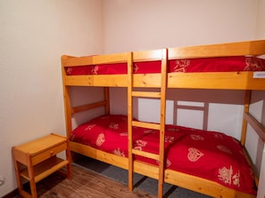 Ein Etagenbett mit roter Bettwäsche und einem kleinen Nachttisch aus Holz.