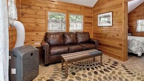 A log cabin interior with a leather sofa, a bench, and a heater. - Ponderosaa - High Mountain Cabin (Spearfish)
