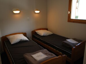 A room with two single beds, each with a pillow and a blanket, and a small table with a folded item on it. - Apartment pets welcome - 6 guests, mountain view (Villarodin-Bourget)