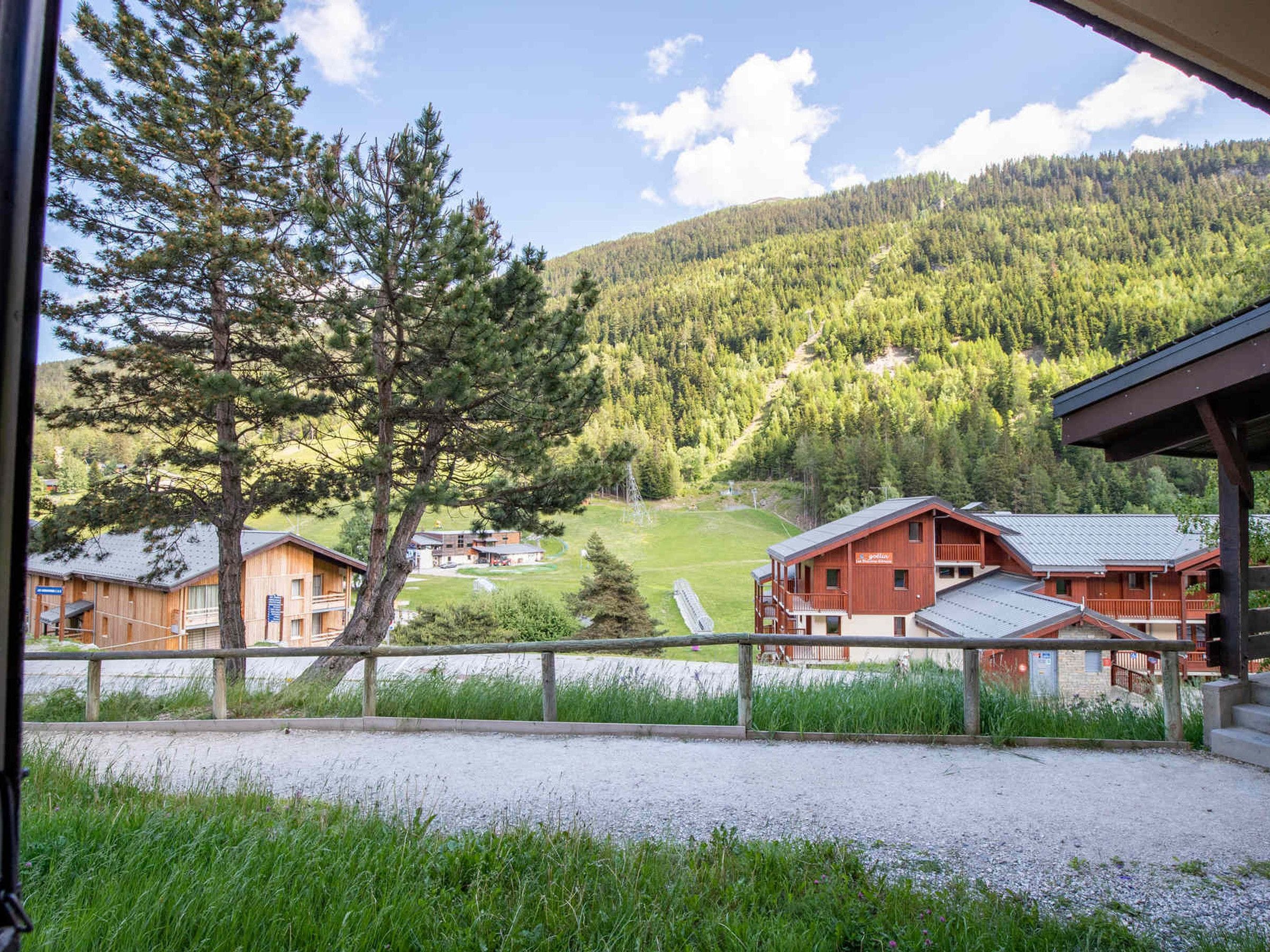 A view of a mountain lodge with multiple wooden buildings, a clear sky, and a forested hillside.