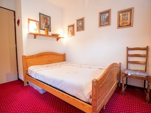 A single wooden bed with a quilt, a chair, and wall-mounted shelves with pictures. - Well-located apartment - 4 guests (Villarodin-Bourget)