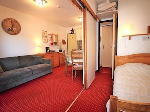 Ein Zimmer mit einer Couch, einem Bett, einem Schreibtisch mit Stuhl, einem kleinen Tisch und einem Spiegel.