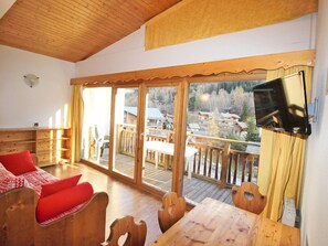 Ein Holzinterieur mit einem Balkon, einem an der Wand montierten Fernseher und Blick auf Häuser in der Ferne.