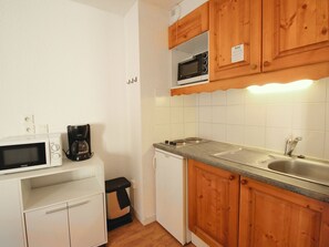 Eine kleine Küche mit weißen Schränken, einer Mikrowelle, einer Kaffeemaschine und einem Spülbecken.