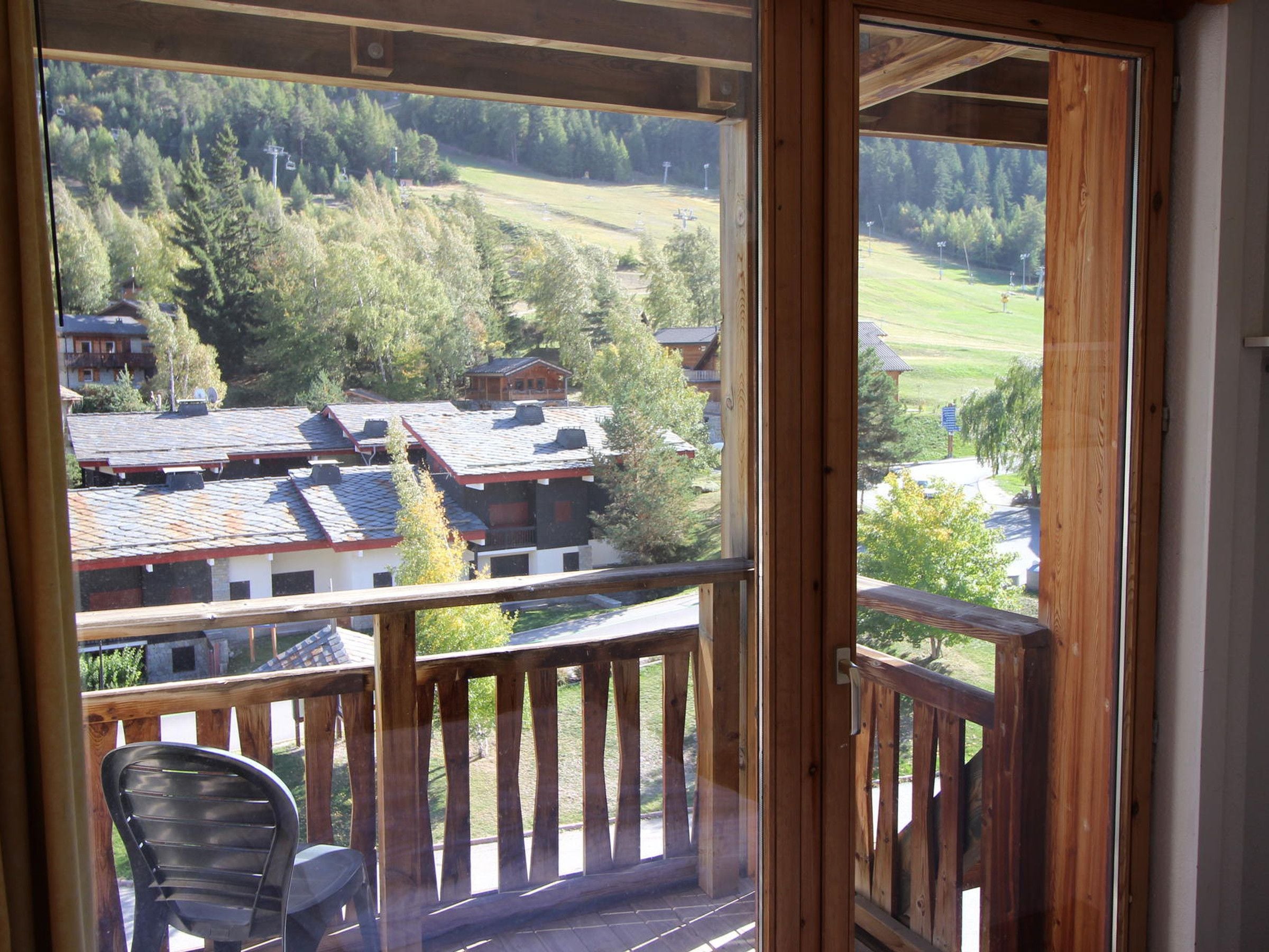 A wooden balcony with a view of a residential area and a chair.