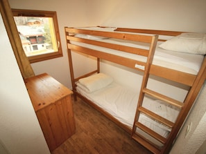 Ein Stockbett mit einem kleinen Holztisch daneben, ein Fenster mit Blick auf Gebäude und eine schlichte Wand.