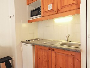 Eine kompakte Küche mit Holzschränken, einer integrierten Mikrowelle, einem Spülbecken und einem Kühlschrank.