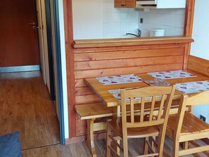 Ein Holztisch mit vier Stühlen, eine Küche mit weißen Schränken und eine Holzbank.