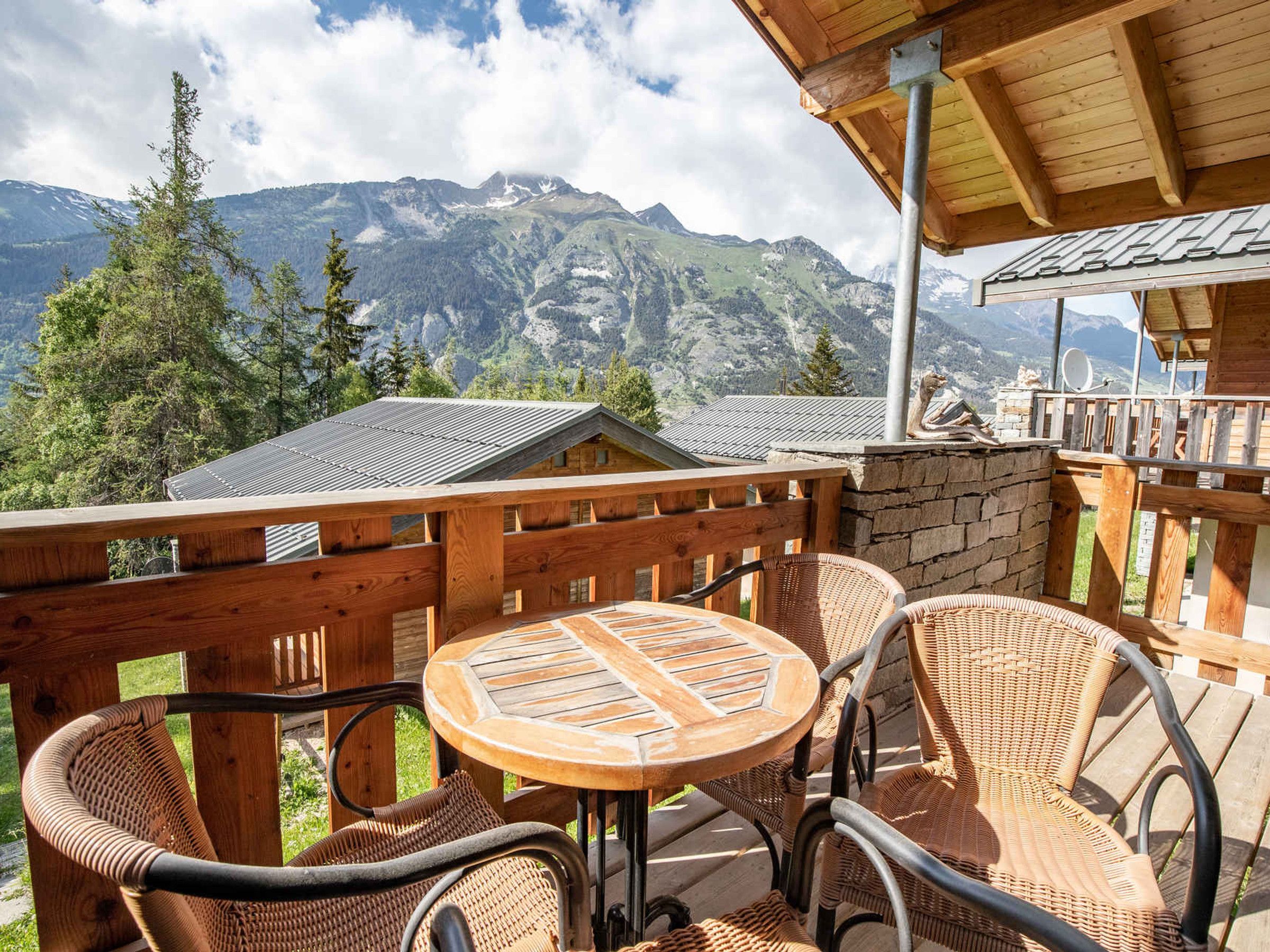 Un terrazzo in legno con mobili in vimini e un tavolo, con vista su un paesaggio montuoso.