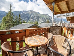 A wooden deck with wicker furniture and a table, overlooking a mountainous landscape. - Quiet duplex chalet, stunning views - 6 guests (Villarodin-Bourget)