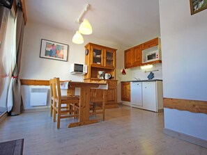A compact kitchen with wooden cabinets, a microwave, a small refrigerator, and a dining area with a wooden table and chairs. - Charming apartment at the foot of the slopes - 4 guests (Villarodin-Bourget)