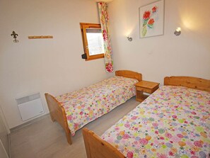 A room with two wooden beds, a window with a curtain, a wall-mounted light fixture, and a radiator. - Charming apartment at the foot of the slopes - 4 guests (Villarodin-Bourget)