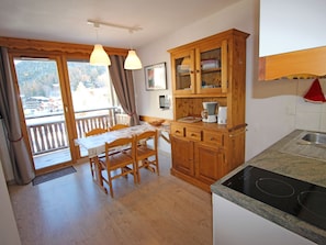 A kitchen with wooden cabinets, a dining table with chairs, a coffee maker, and a view through the window. - Charming apartment at the foot of the slopes - 4 guests (Villarodin-Bourget)
