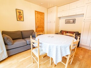 A dining area with a round table, chairs, a grey sofa, wooden cabinets, and a wooden door. - Apartment mountain view - 6 guests (Villarodin-Bourget)