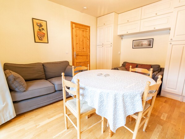 En matplats med ett runt bord, stolar, en grå soffa, träskåp och en trädörr.