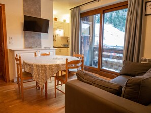 A cozy living area with a dining table, chairs, a sofa, and a TV mounted on the wall. - Apartment mountain view - 6 guests (Villarodin-Bourget)