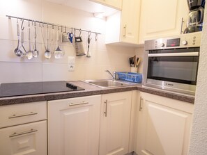 A kitchen with white cabinets, a Bosch oven, and various utensils hanging on a rack. - Apartment mountain view - 6 guests (Villarodin-Bourget)