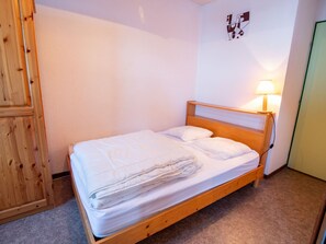 Ein Einzelbett mit Holzrahmen und weißer Bettwäsche, eine Nachttischlampe und eine Wand mit einem geometrischen Kunstwerk.