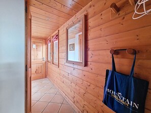 A wooden hallway with a tiled floor, a door on the left, and a blue bag hanging on the wall. - Spacious apartment with balcony and parking, close to slopes - 6 people (Les Menuires)