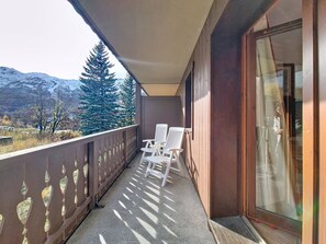 Un balcon avec des chaises blanches, une vue sur des montagnes enneigées et une porte vitrée.