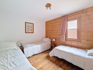 Une chambre avec deux lits, une fenêtre avec des rideaux, un luminaire fixé au mur et un tableau encadré.