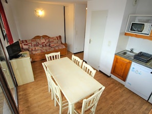 Een praktische keuken met een eettafel, stoelen, een magnetron en een kleine koelkast.