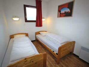 Een kamer met twee houten bedden, een raam met gordijn, een wandlamp en een lijst met een afbeelding.