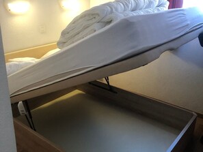 A bed with a mattress and pillows, a wooden drawer below, and a wall with a light fixture. - Apartment with mountain view - 6 guests (Villarodin-Bourget)