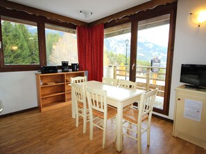 Un espace repas comprenant une table et des chaises, un coin café, un téléviseur et une vue sur les montagnes grâce à de grandes fenêtres.