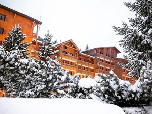 Un edificio de madera de varios pisos con balcones, rodeado de árboles cubiertos de nieve.