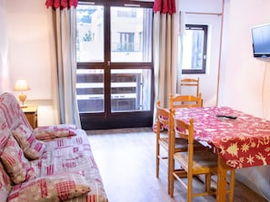 A room with a sofa, a dining table with chairs, a TV on the wall, and a window with curtains. - Mountain-style apartment, pets welcome - 4 guests (Villarodin-Bourget)