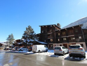 A multi-story building with a wooden facade, a parking lot with several cars, and a snow-covered landscape. - Mountain-style apartment, pets welcome - 4 guests (Villarodin-Bourget)