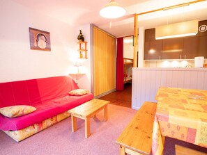 A cozy room with a red sofa, a wooden table, and a small kitchenette area. - Ideal studio slopeside, pets welcome - 4 guests (Villarodin-Bourget)