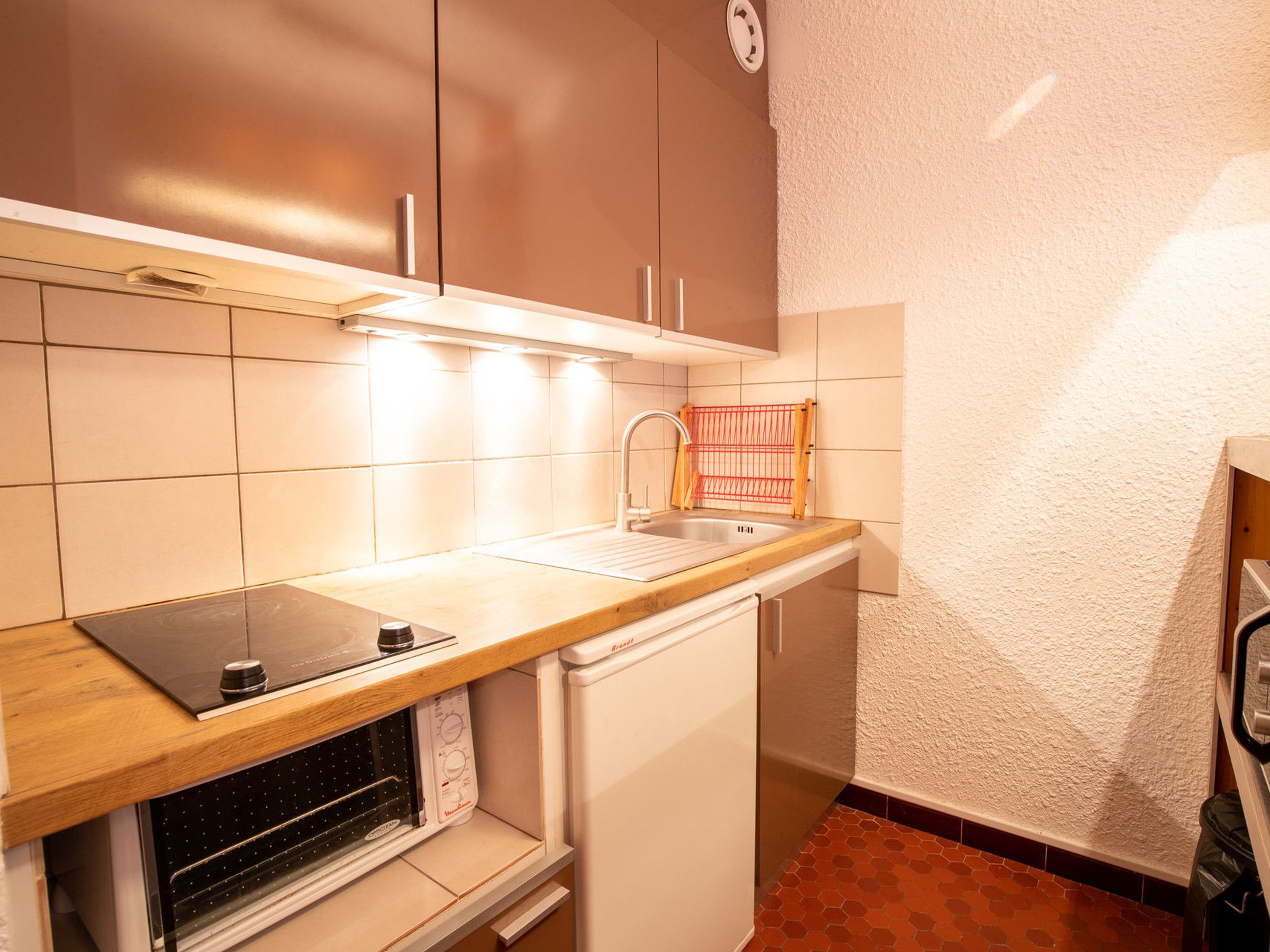 Una cucina compatta con forno a incasso, lavello e microonde.