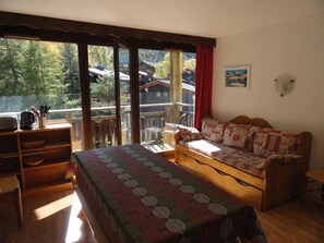 A room with a bed, a desk, and a view of a forest and buildings. - Spacious apartment mountain view - 10 guests (Villarodin-Bourget)
