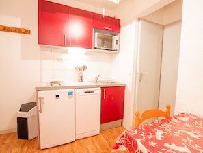 A compact kitchen with a microwave, a dishwasher, and a sink. There is a small trash bin and a wooden chair. - Cozy apartment, pets welcome - 4 guests (Villarodin-Bourget)