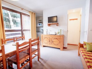 A room with a wooden dining table and chairs, a kitchenette with a microwave, a television on a stand, and a door leading to another room. - Apartment, pets allowed, mountain view - 6 guests (Villarodin-Bourget)