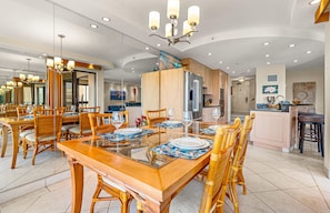Een ruime eethoek met een lange houten tafel, rieten stoelen en een moderne kroonluchter.